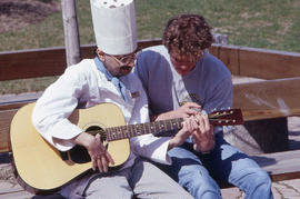 Photograph of a Hospitality student demonstrating fingering on a guitar to another student