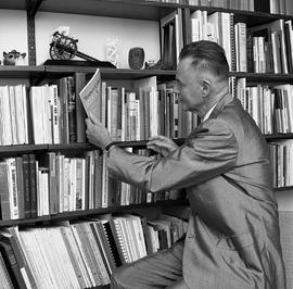 Photograph of J. Roby Kidd pulling a magazine from the bookshelf