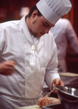 Photograph of culinary student tying a stuffed pork roast in preparation for cooking