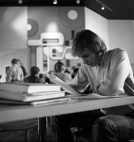 Photograph of a student reading a paper in the concourse of the E building