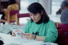 Photograph of a student reading a pamphlet about 'Adult Immunization' in the library
