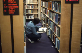 Photograph of a Student Browsing a Book in the Library Stacks