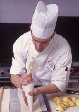 Photograph of a culinary student using a piping tool to extrude dough onto parchment paper