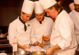 Photograph of students chefs putting their heads together for a dish