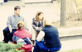 Photograph of students sit on the curb in the courtyard behind building "E"