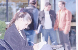 Photograph of a student studying outside while others converse in the background