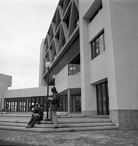 Photograph of two students sitting on the stairs outside behind the E building