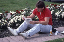 Photograph of student reading SAC student handbook by flowers