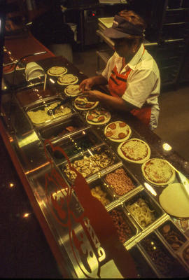 A photograph of a staff member preparing pizzas in the cafeteria
