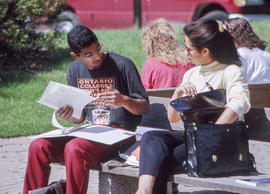 Photograph of students seated on a bench and discussing an assignment