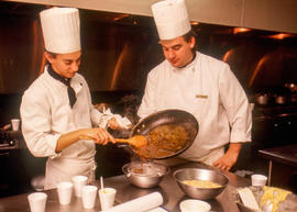 Photograph of two Culinary students straining sauce from a pan