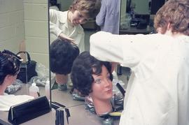 Hairdressing student works on styling hair on a dummy : [photograph]