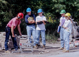 Photograph of a group of students observing their professor using a stone cutter