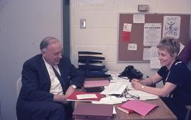 School President Gordon Wragg sitting at desk with staff member : [photograph]