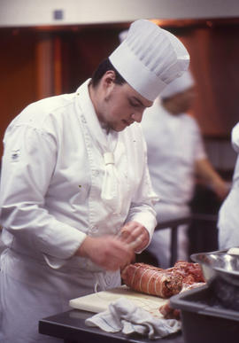 Photograph of a Culinary program student tying a roast