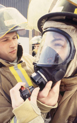 A photograph of a Firefighting student assisting another in head gear