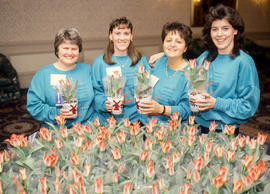Photograph  of four persons holding a tulip plant in hand