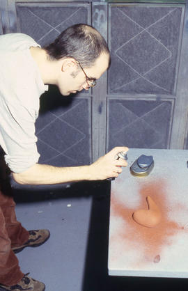 A photograph of a student spray painting one of their designs