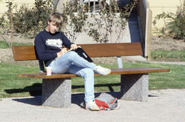 Photograph of a student studying while on a bench by the Arboretum