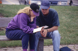 Photograph of Two Students Looking at Sheets By the Greenhouse