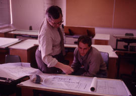 Photograph of instructor inspecting student's work on a drafting table