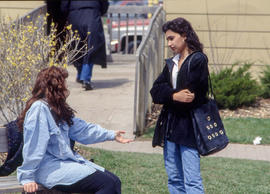 Photograph of two students conversing at a bench on campus