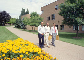 Photograph of three men walking by Building B at Lakeshore campus