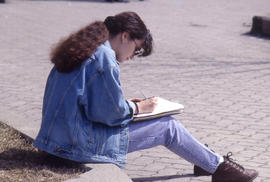 Photograph of a Girl Writing Notes on a Curb