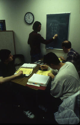 A photograph of a faculty member writing on a chalkboard
