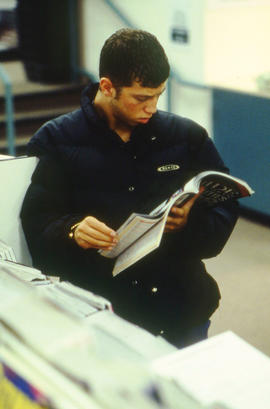 Photograph of a student flipping  through a magazine by a rack in the Bookstore