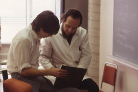 Photograph of an instructor and student referencing information from textbook