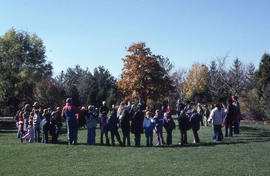 Photograph of large group of children and adults gather in a circle in the Arboretum
