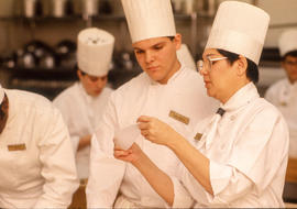 Photograph of a Culinary student being shown how to fold paper for piping.
