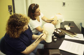 A photograph of two Funeral Services students practice on their mannequins in a lab