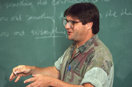 Photograph of Paul Quarrington with chalk in hand standing by a blackboard