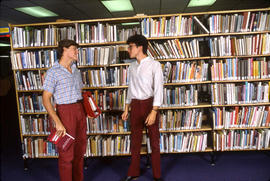 Photograph of Two Students Talking in the Library by the Bookshelf