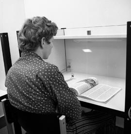 Photograph of a student reading a magazine in the study carrel in the library