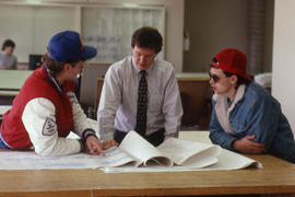 Photograph of drafting instructor looking at drawings with two students