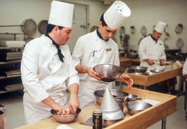 Photograph of two student chefs following a recipe and mixing ingredients
