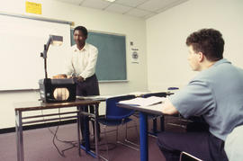 A photograph of a student watching their professor use an overhead projector