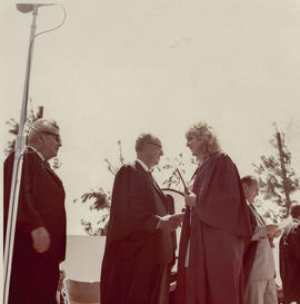 Photograph of a graduate being congratulated by a member of the board of governors at a Convocation