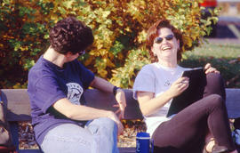 A photograph of two students laughing while sitting on a bench