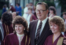 Photograph of two graduates in gowns posing with an unknown person