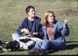 Photograph of two friends seated on the lawn on campus