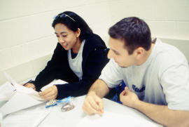 Photograph of students sitting at a desk in a classroom reviewing notes