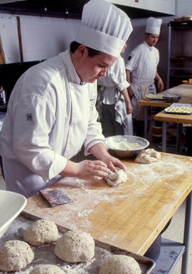 Photograph of students in their chef uniform kneading dough