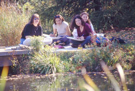 Photograph of students sitting near the pond in the Arboretum