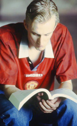 Photograph of a student sitting in an unknown location reading a textbook