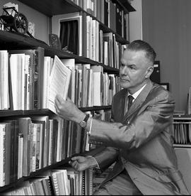 Photograph of J. Roby Kidd pulling a magazine from the bookshelf