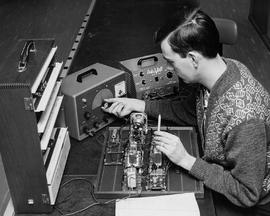 Photograph of an electronics student adjusting a laboratory generator while working on a piece of...